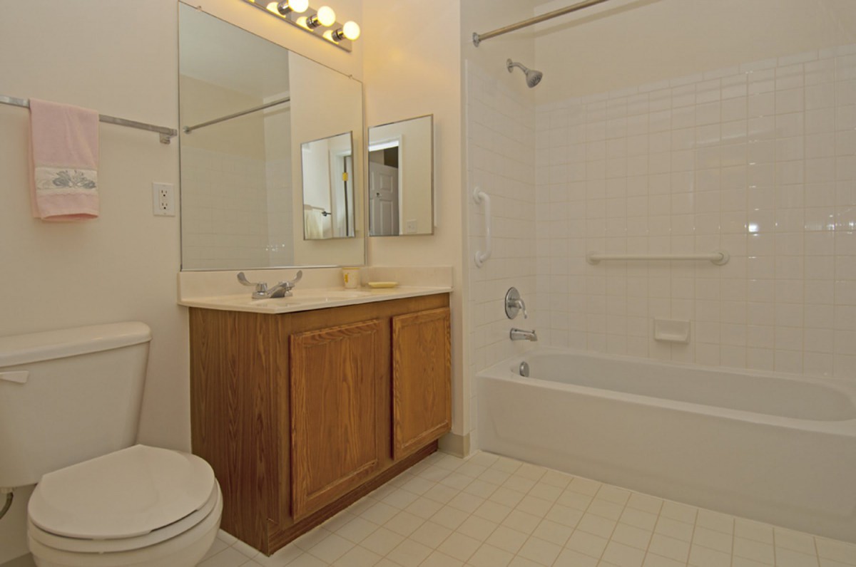A clean and simple bathroom with a wooden vanity, a large mirror, and a bathtub.