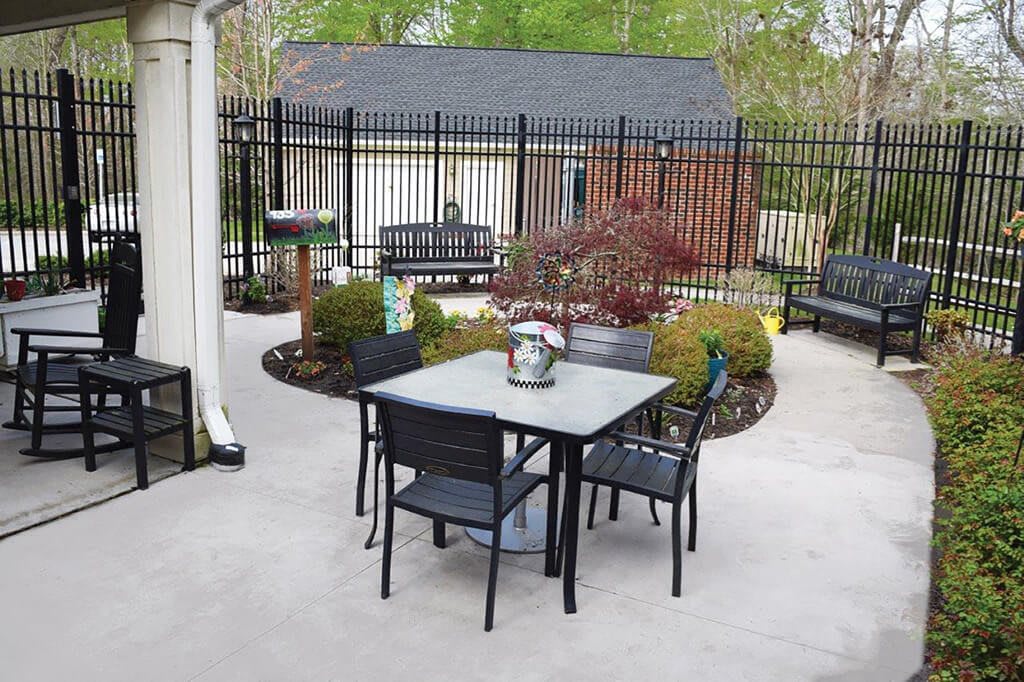 A cozy outdoor patio area with a table and chairs surrounded by greenery.