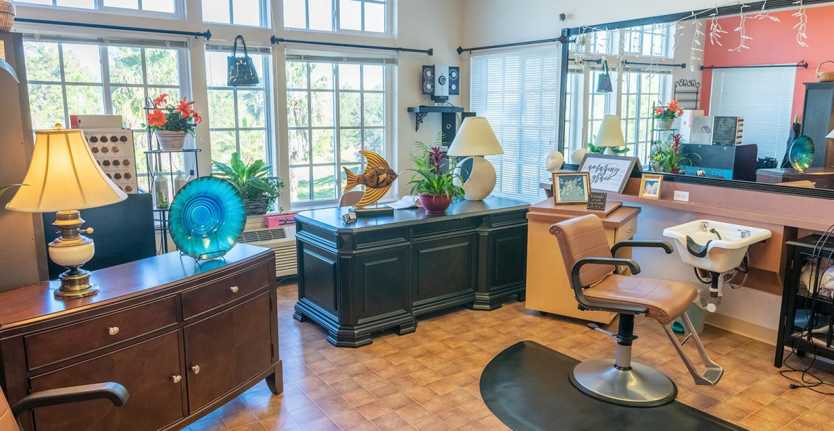 A bright office space featuring a large black desk, comfortable chair, and decorative elements under ample natural light from the windows.