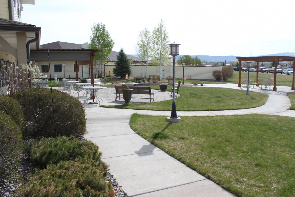 A tranquil park area featuring pathways, benches, and outdoor seating surrounded by greenery.