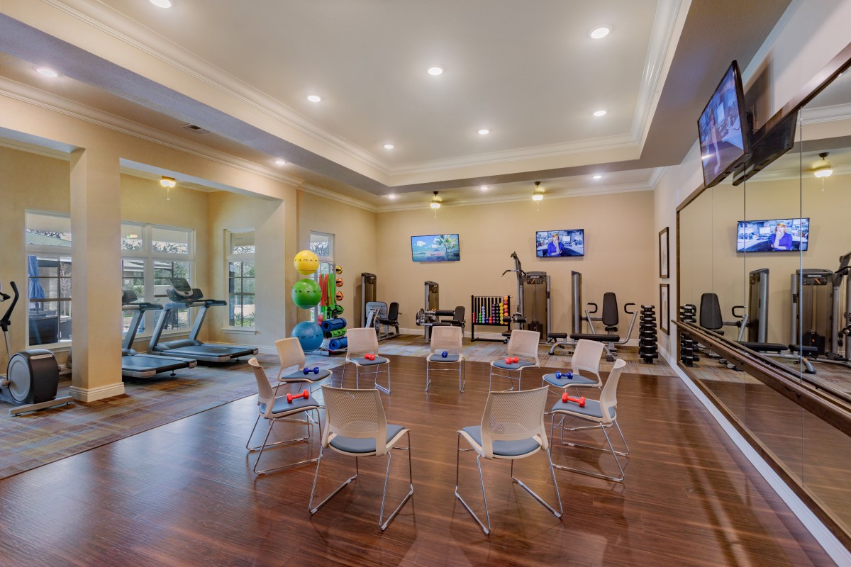 A spacious gym with exercise equipment, including treadmills and bikes, mirrors, and televisions on the walls.