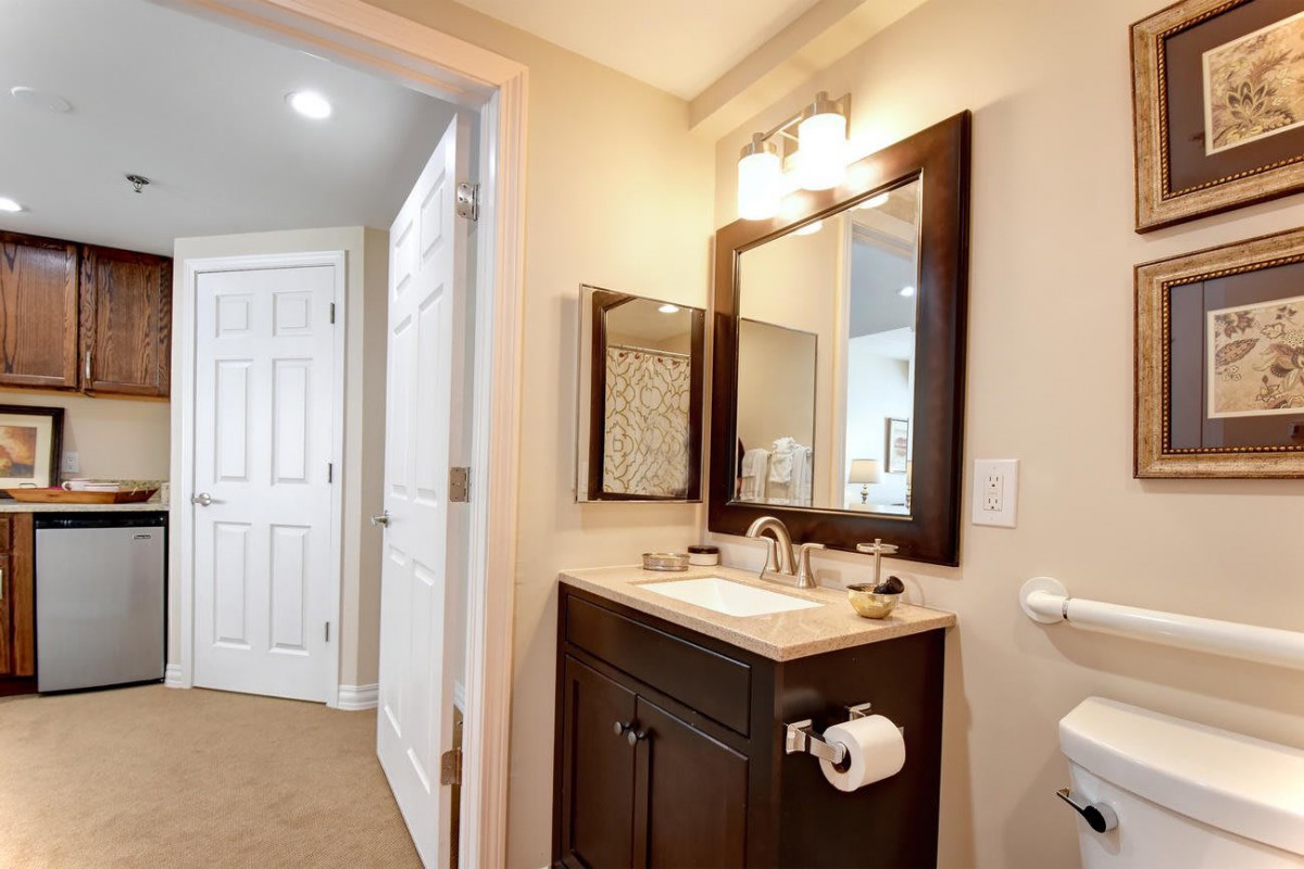 A neatly designed bathroom with a dark wood vanity, featuring a large mirror and overhead lighting.