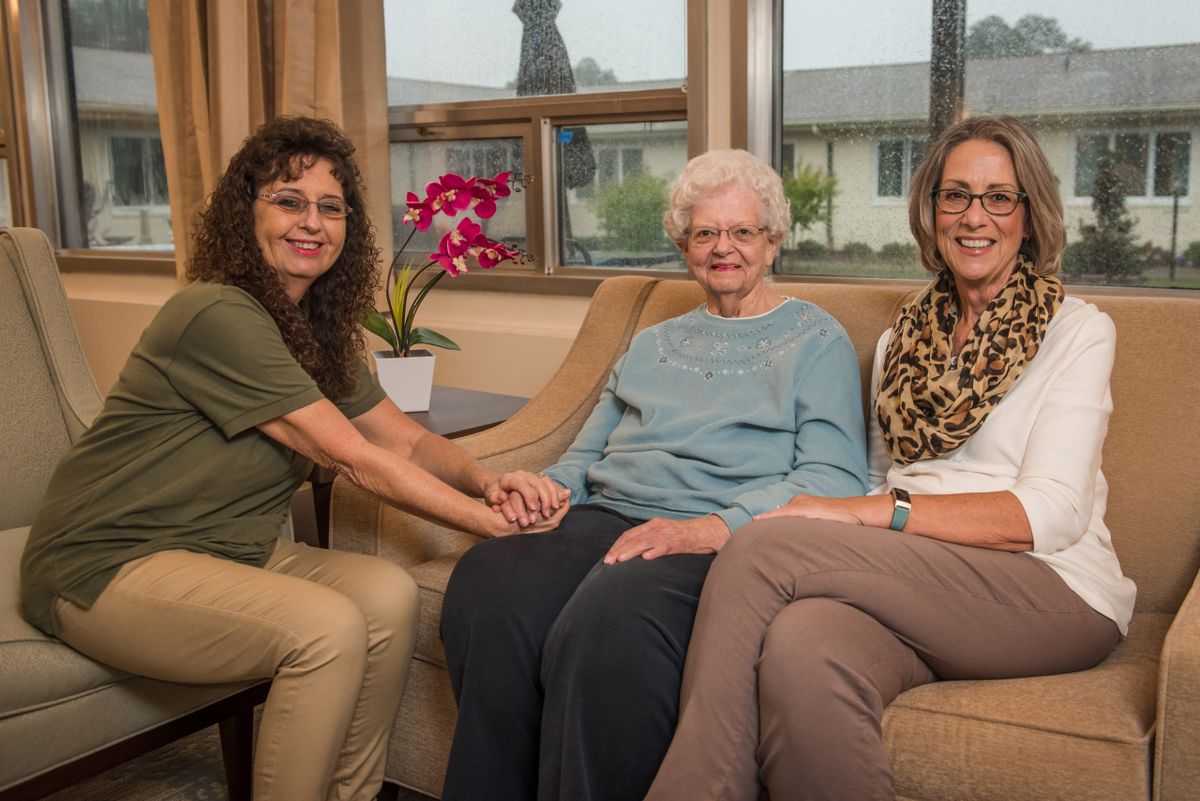 Three women sitting together in a living room, smiling at the camera.
