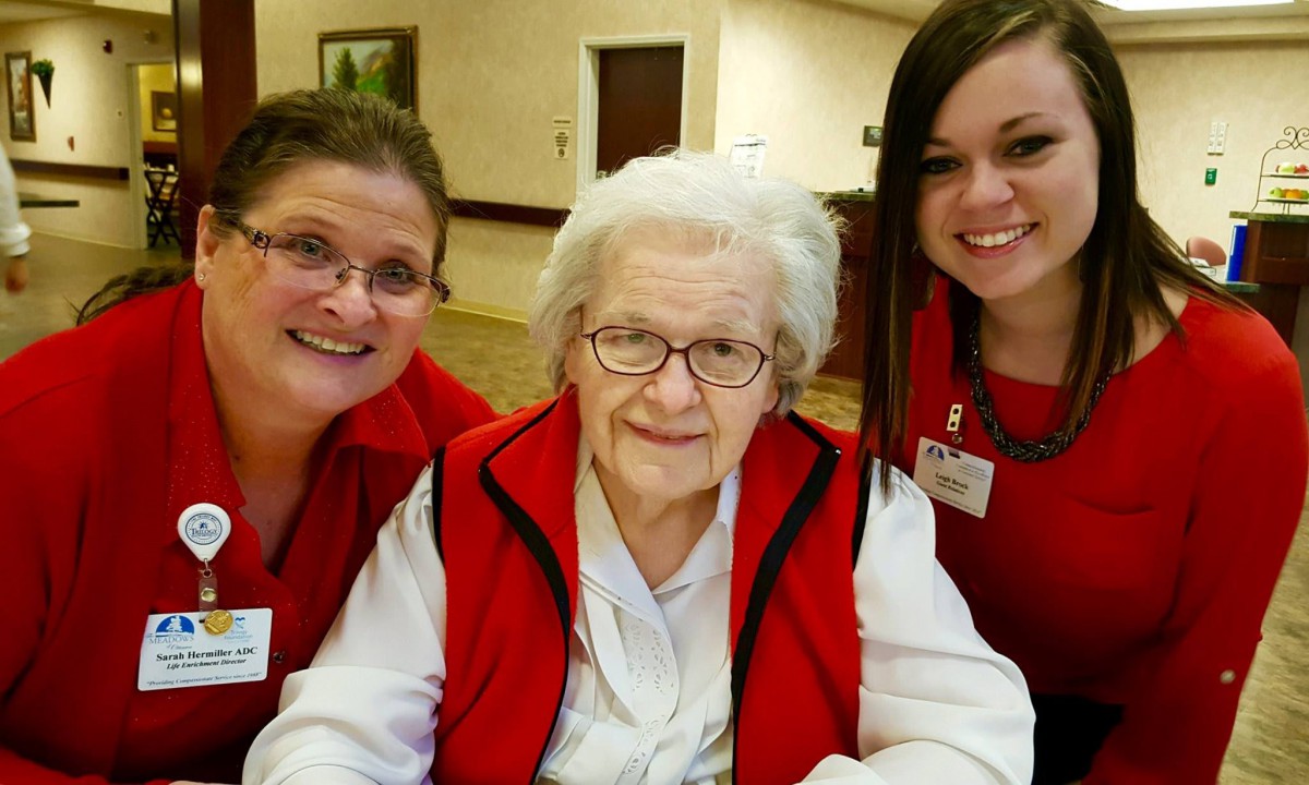 An elderly woman seated between two smiling women, all wearing red vests.