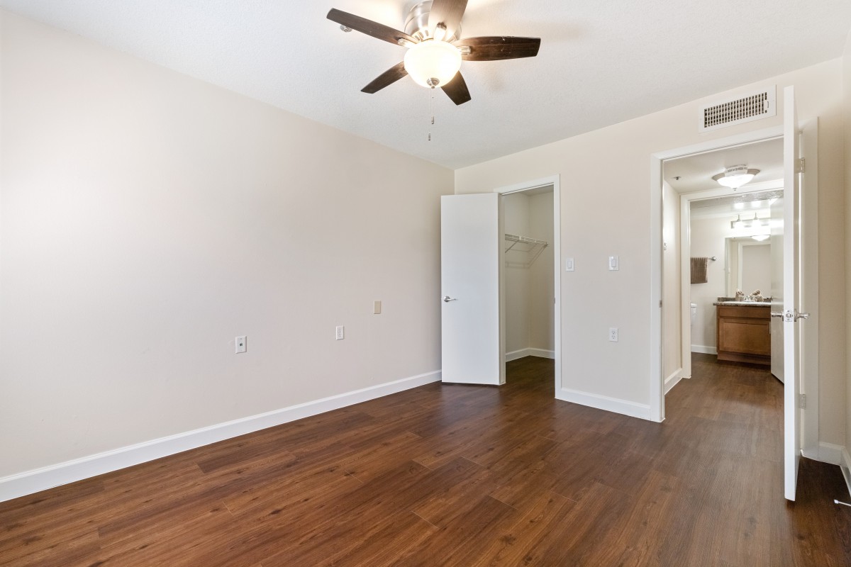 An empty room with wooden flooring and a ceiling fan, featuring an open door leading to a closet and hallway.