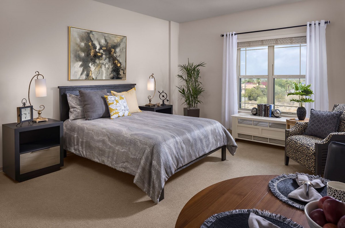A modern bedroom with stylish decor, featuring a large bed, artwork, and a window with natural light.