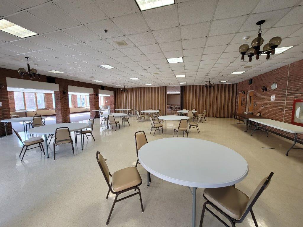 An empty meeting hall with round tables and chairs arranged in an orderly fashion.