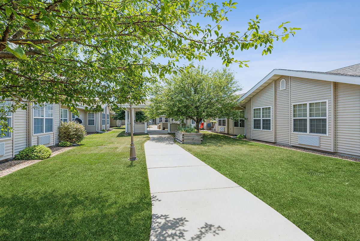 A peaceful outdoor pathway leading between buildings surrounded by trees and grass.