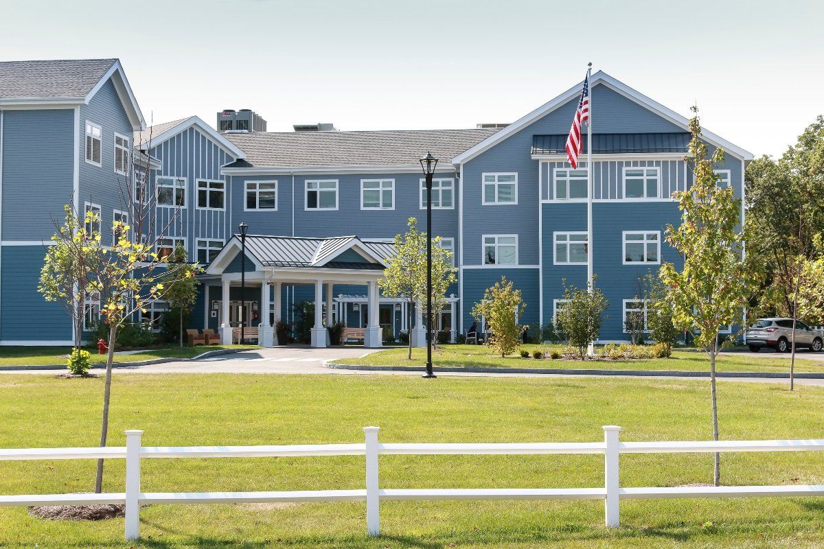 A large blue residential building with a well-maintained lawn and white picket fence, featuring an American flag on display.