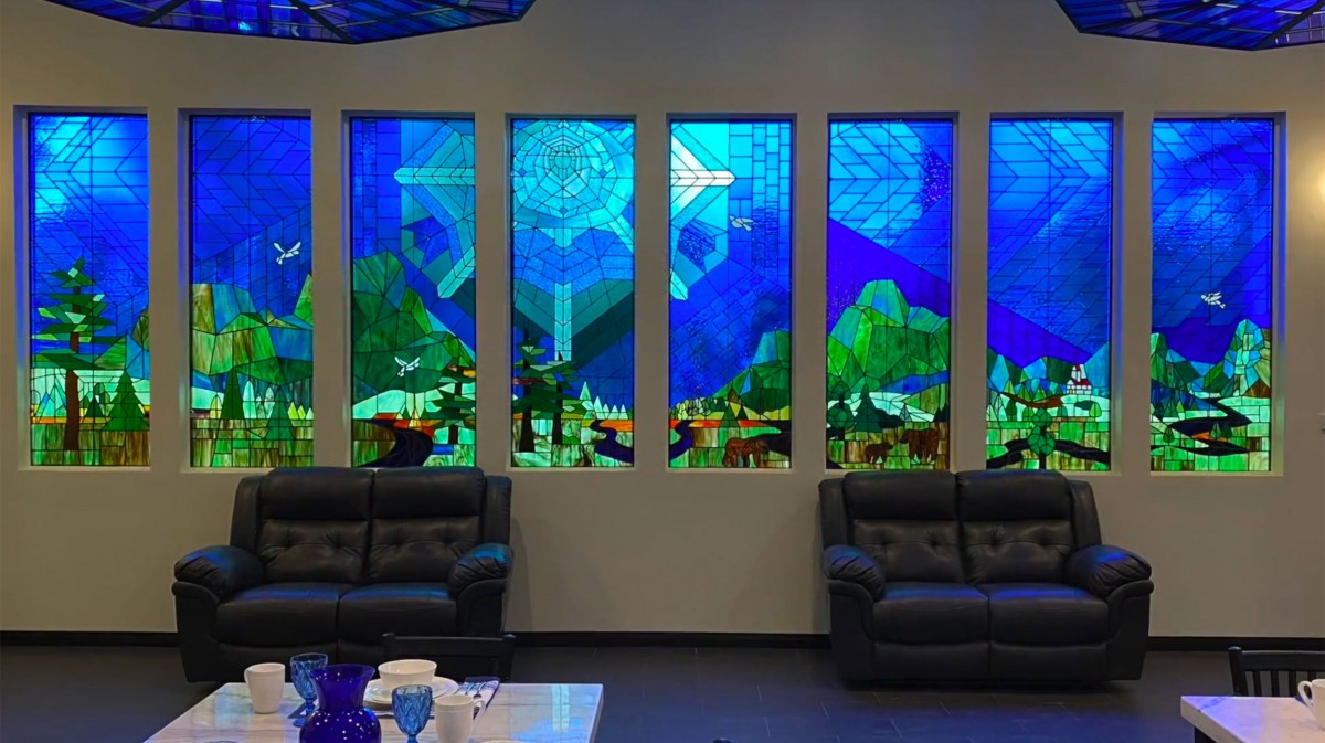A room featuring vibrant stained glass windows with a scenic design, complemented by comfortable sofas.