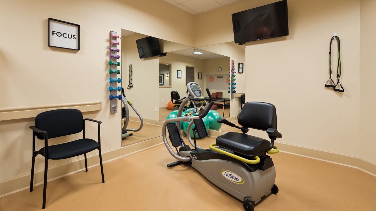 A well-equipped therapy room featuring a stationary bike, exercise balls, and mirrors.