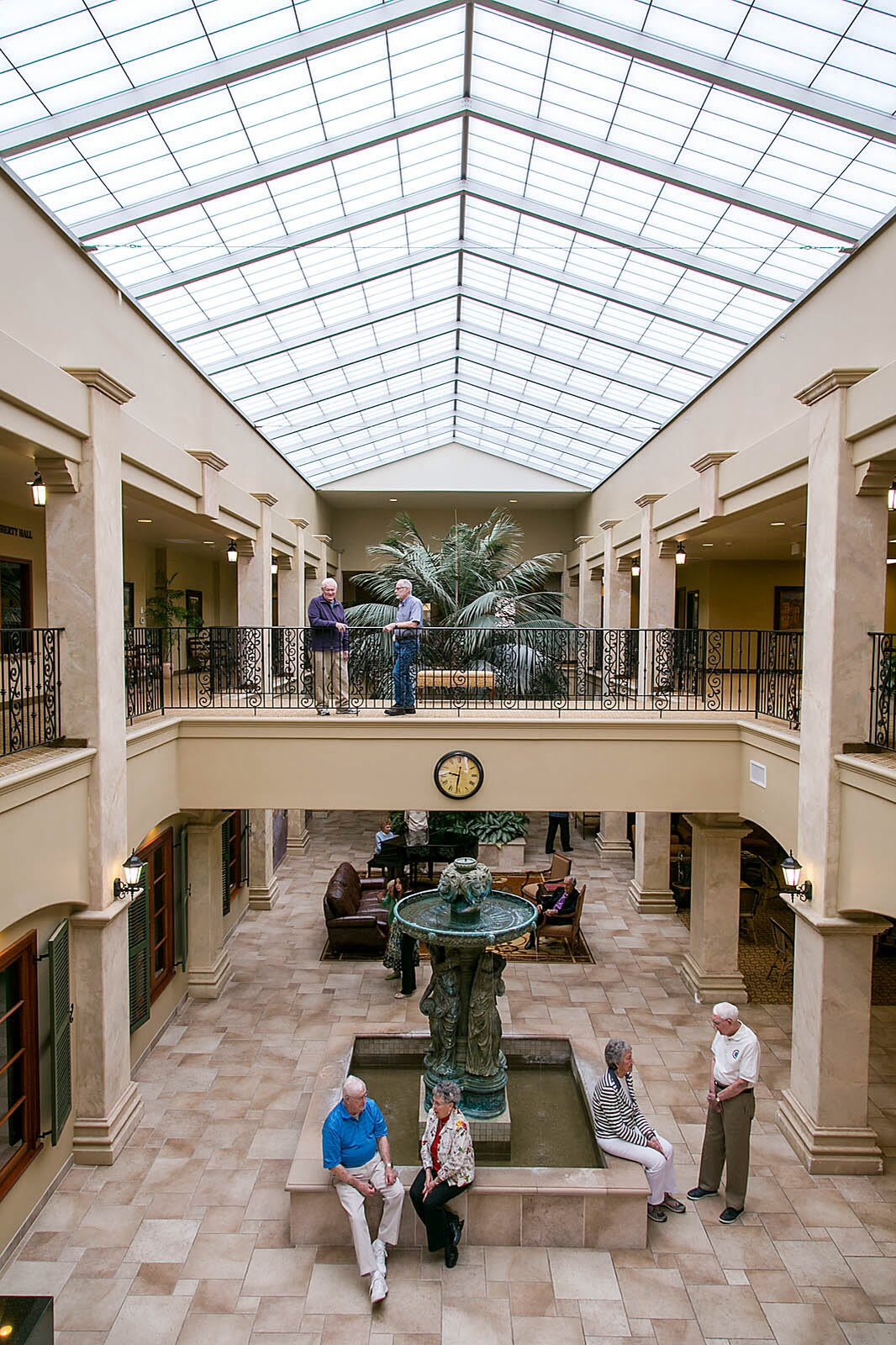 A spacious atrium with a skylight, featuring a central fountain and surrounding balconies with people interacting.