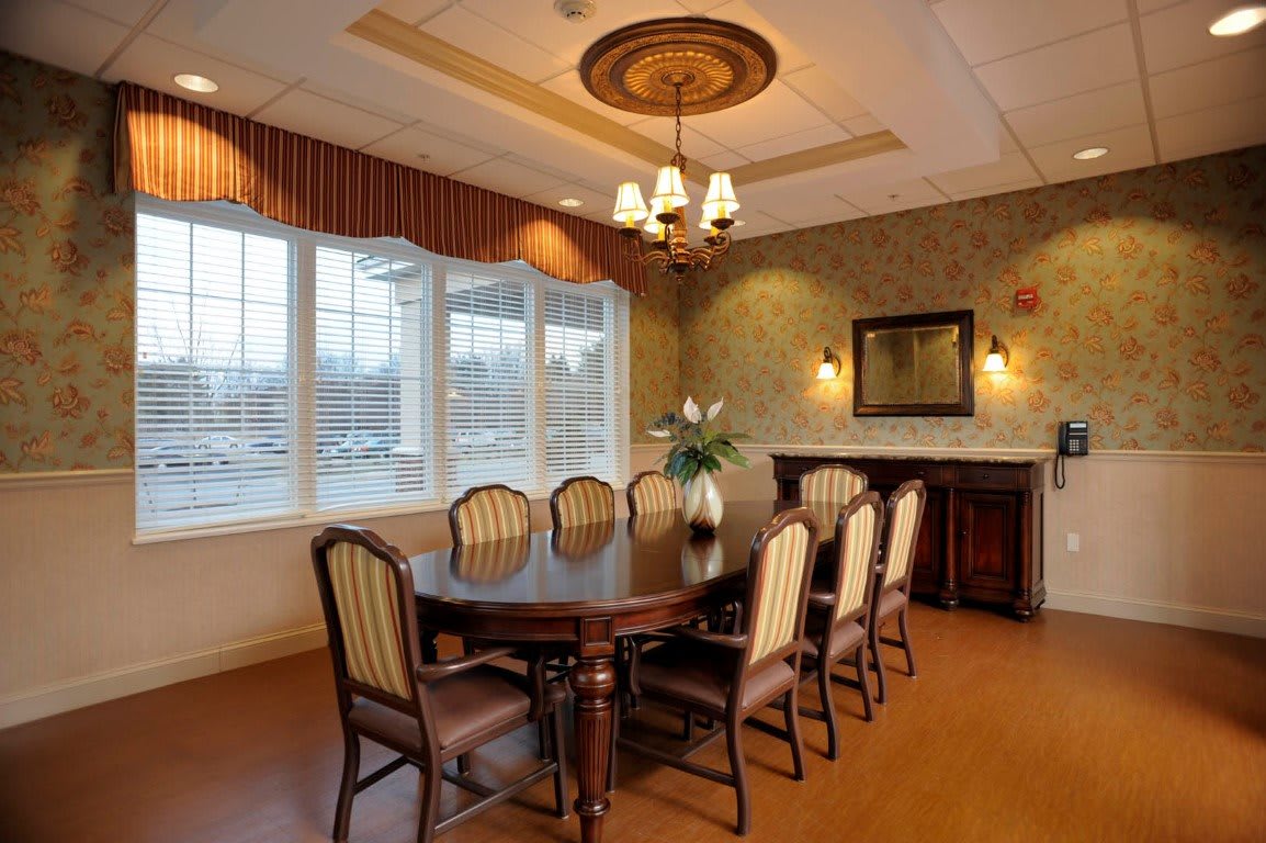 An elegantly designed dining room with a large table and chairs, featuring a chandelier and a window allowing natural light.