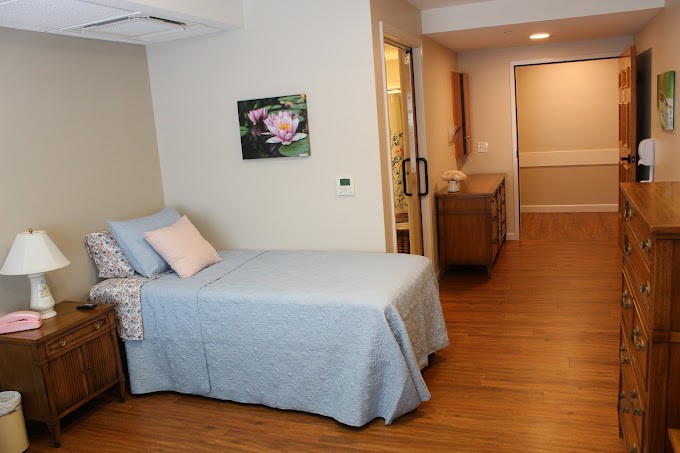 A clean and minimalist hospital room featuring a single bed with a light blue cover and wooden flooring.