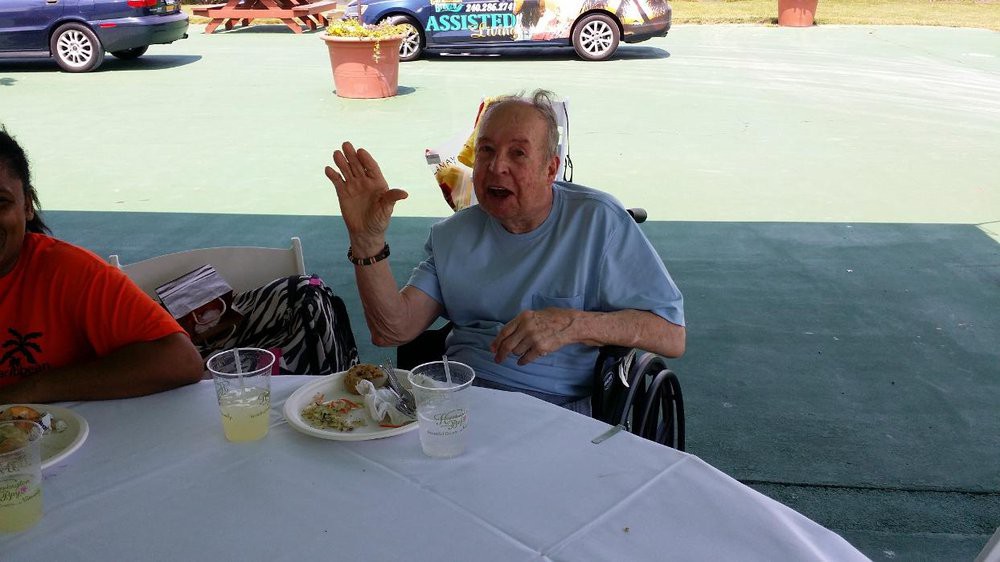 An elderly person in a wheelchair enjoying a meal outdoors at a table.