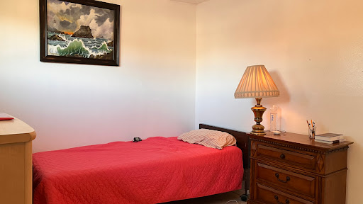 A cozy bedroom featuring a bed with red bedding, a bedside lamp, and wall art.