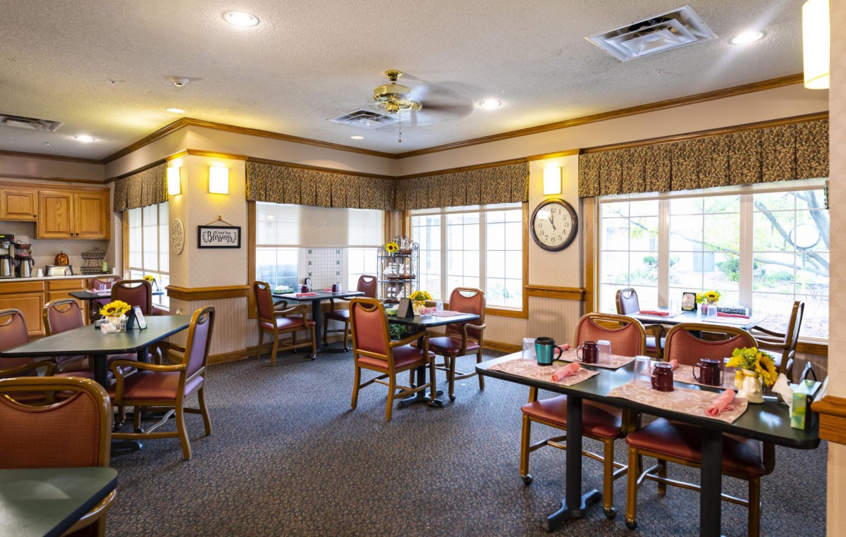 A cozy dining area with multiple tables and chairs, featuring large windows and warm lighting.