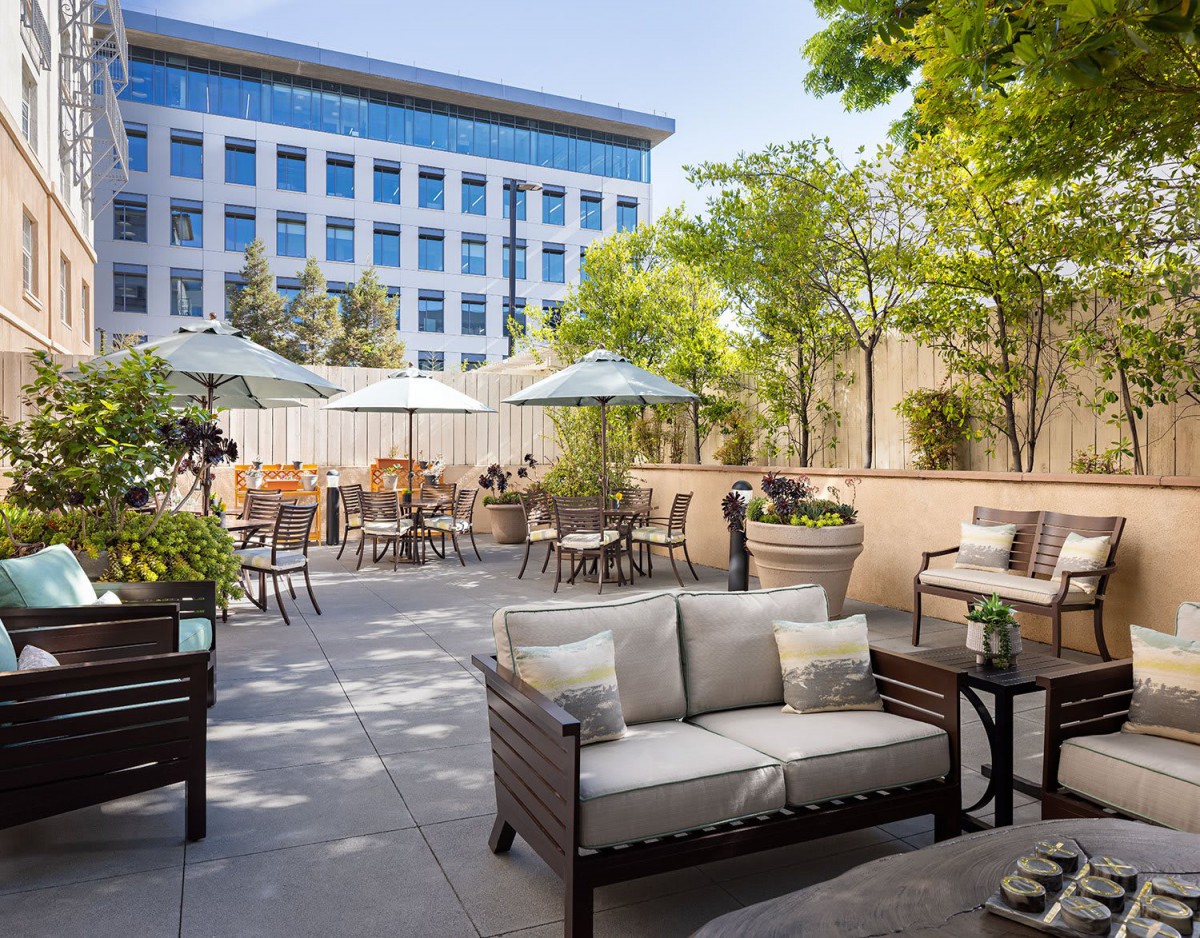 An inviting outdoor patio featuring comfortable seating, tables with umbrellas, and greenery in an urban setting.