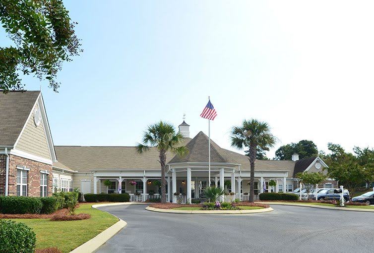 A clubhouse with a circular driveway, featuring palm trees and an American flag at the entrance.