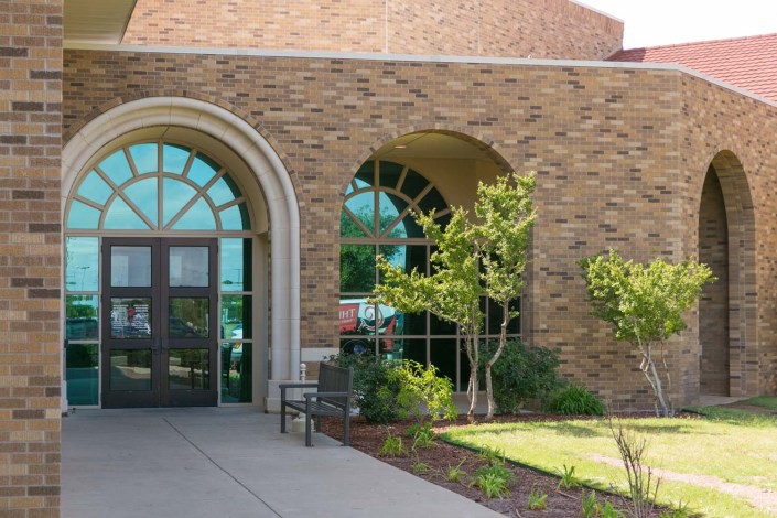 The entrance of a brick building with arched windows and well-maintained landscaping.