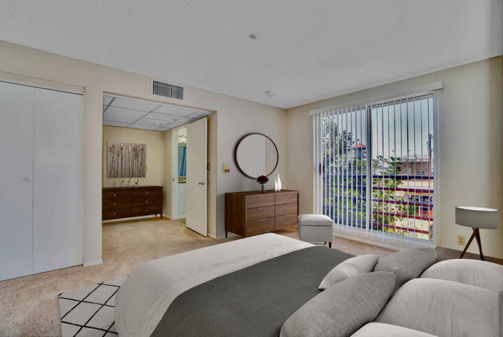 A modern bedroom interior featuring a bed, dresser with a mirror, and large windows with vertical blinds.