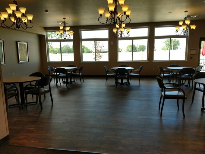 An empty dining room with tables, chairs, and chandeliers, featuring large windows.