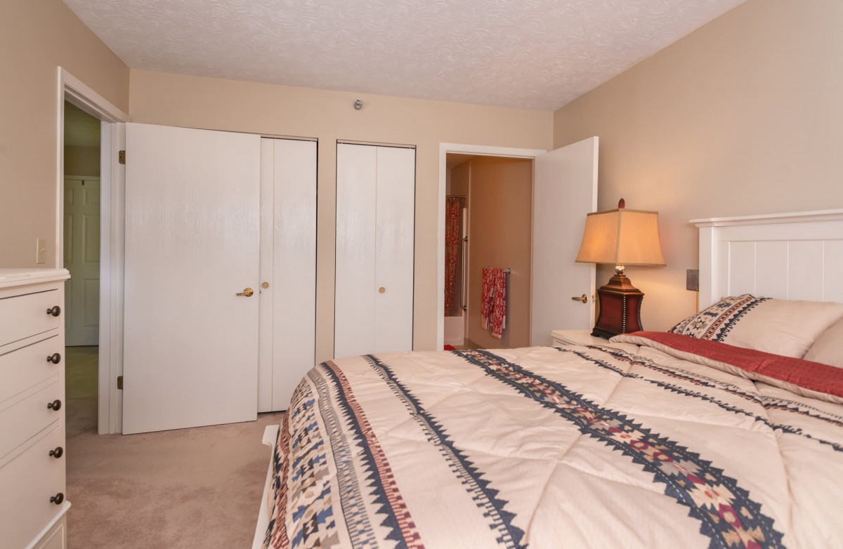 A cozy bedroom with a bed, lamp, and closet doors.