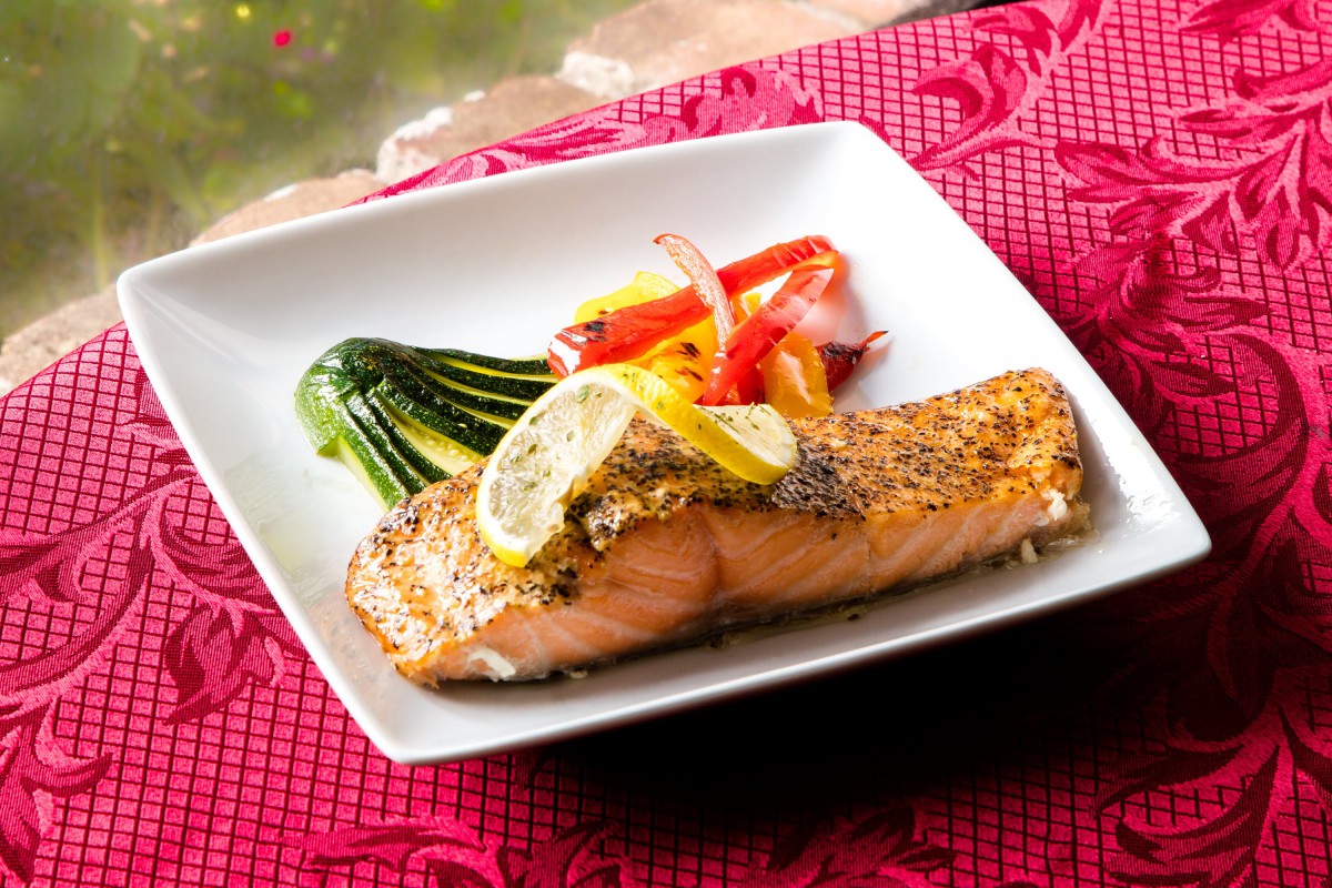 A beautifully plated grilled salmon fillet served with lemon slices and a side of roasted vegetables including zucchini and peppers.