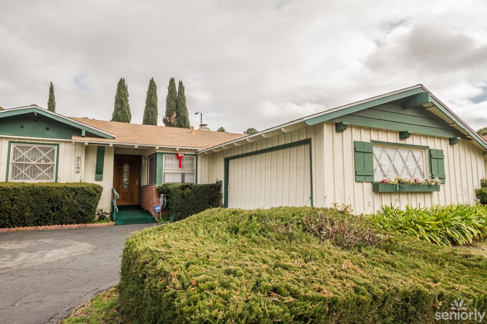 A suburban house with green accents and a well-maintained yard under a cloudy sky.