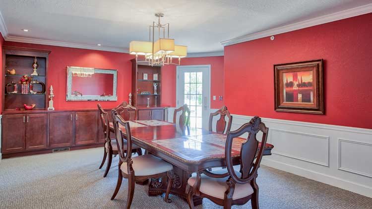 A formal dining room with a long wooden table and elegant chairs, featuring red walls and a chandelier.