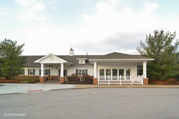 A white single-story building with a driveway and several windows, set against a cloudy sky.