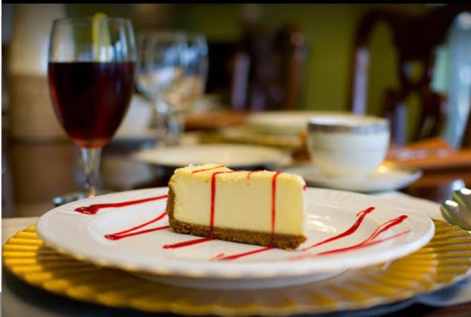 A slice of cheesecake drizzled with raspberry sauce on a plate, set on a dining table.