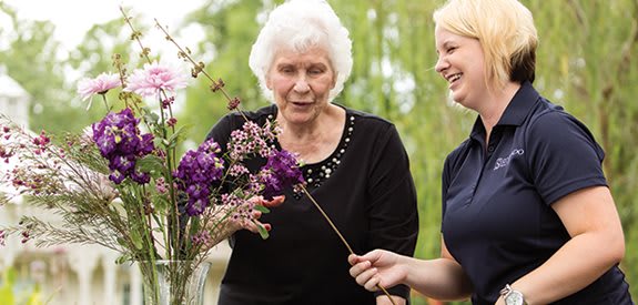An elderly woman and a younger woman arranging flowers together outdoors.