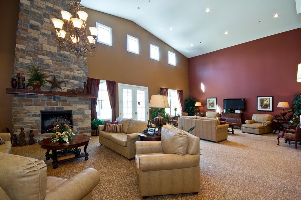 Spacious living room featuring a high ceiling, elegant chandelier, and a cozy fireplace, with comfortable sofas and armchairs for seating.