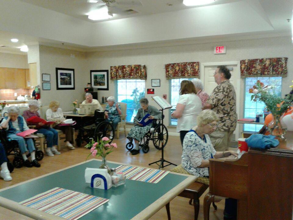 A group of elderly individuals participating in a communal activity at a nursing home, with one person playing the piano.