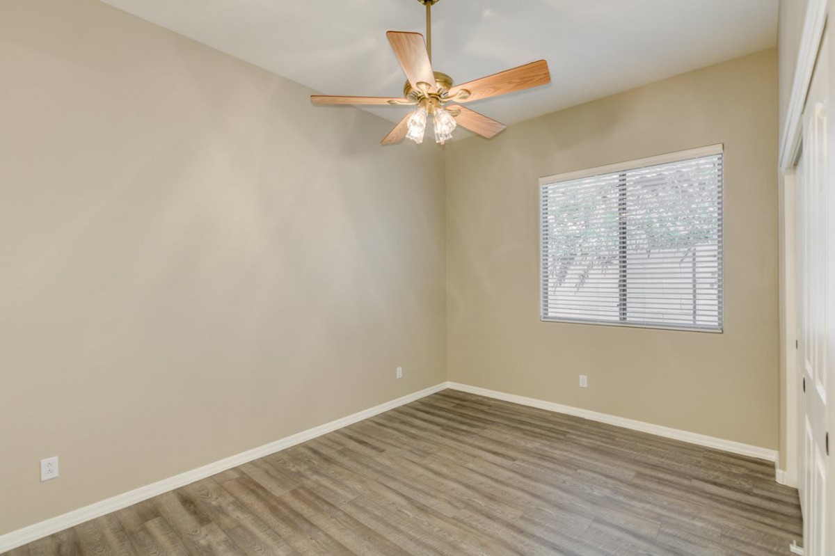 An empty room featuring a ceiling fan, wood flooring, and a window with beige-colored walls.