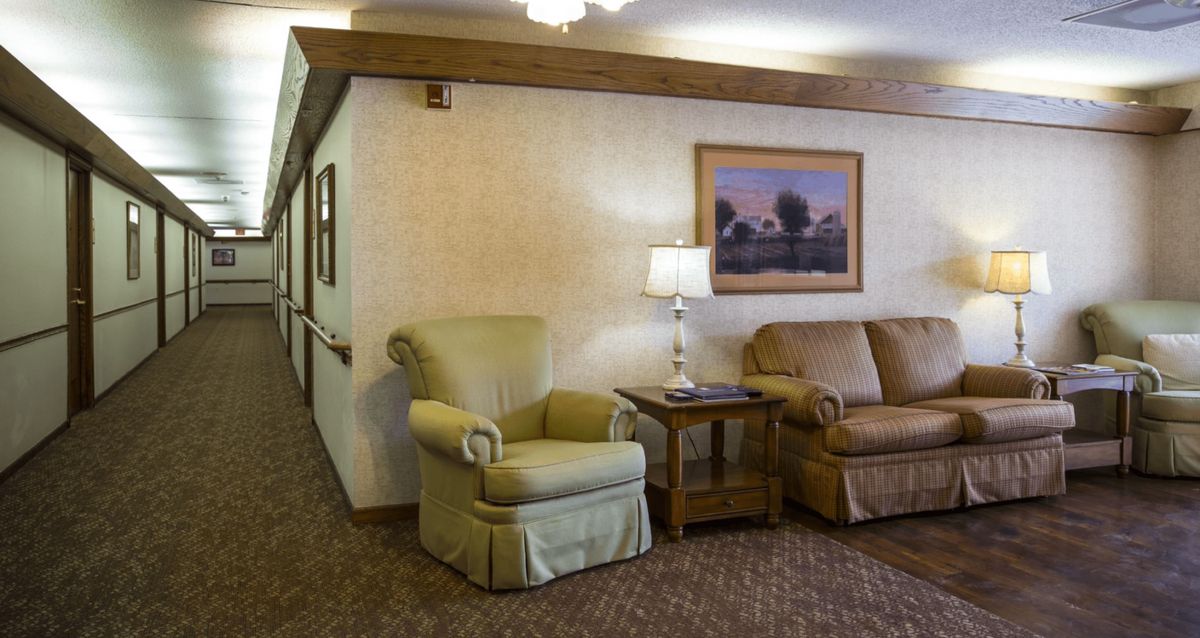 A cozy living room corner with an armchair, sofa, and a side table with a lamp.
