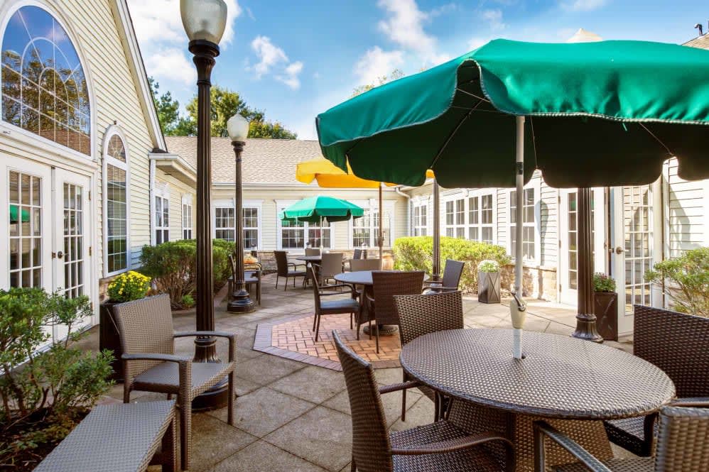 A sunny outdoor patio with several tables and chairs, shaded by green and yellow umbrellas.