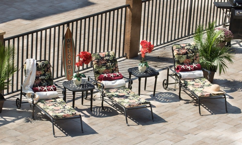 An inviting patio setup with lounge chairs and tables adorned with floral cushions and decorative flowers.