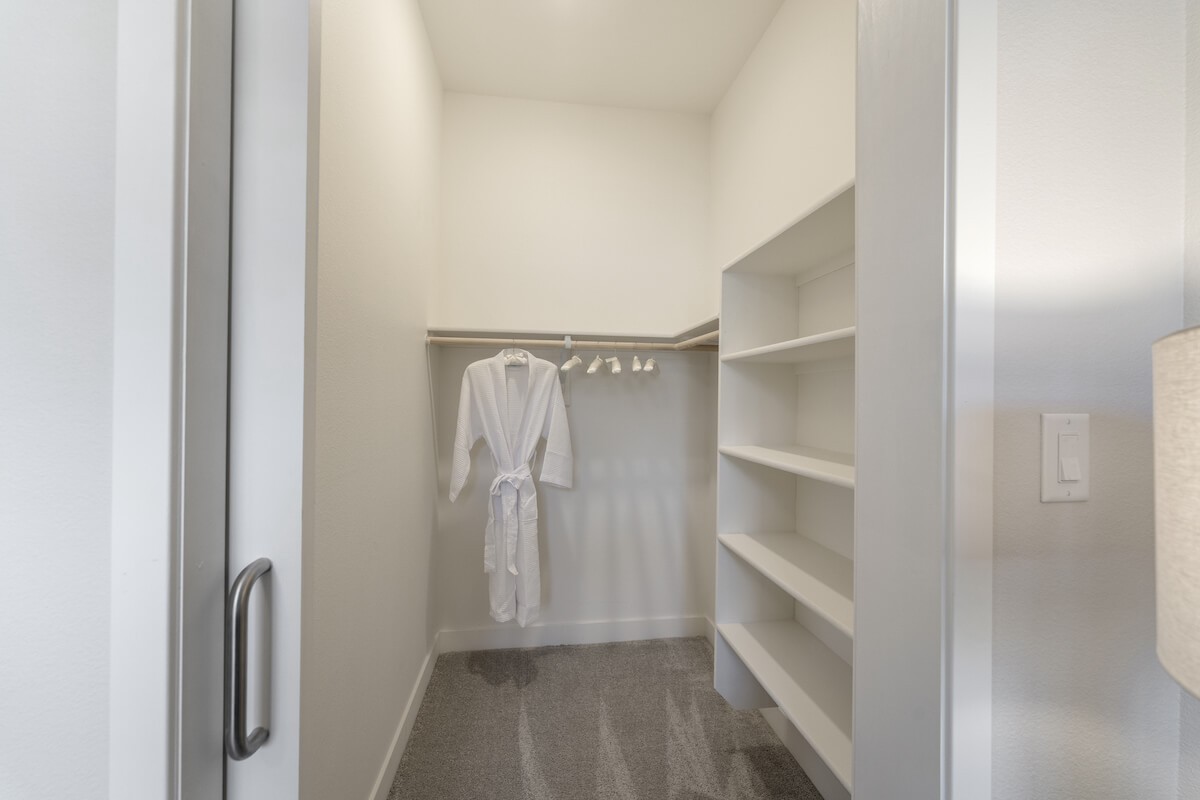 A minimalist walk-in closet with open shelves and a white robe hanging.