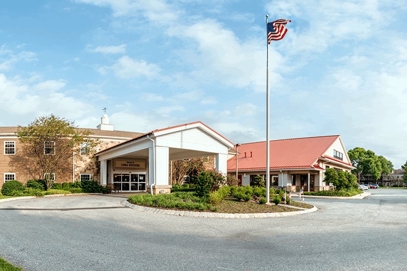 A building with a peaked roof and an American flag flying in front, surrounded by landscaping and under a clear blue sky.