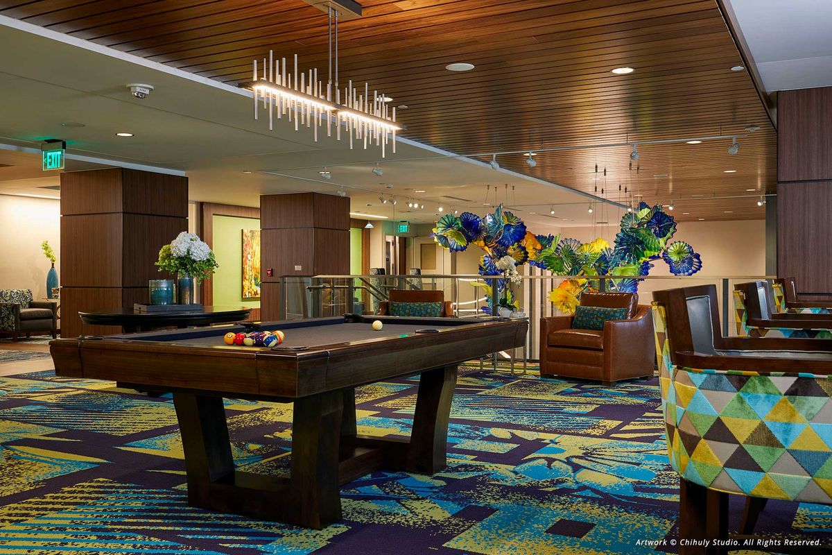 A modern indoor lounge featuring a pool table, colorful carpet, and decorative balloons.