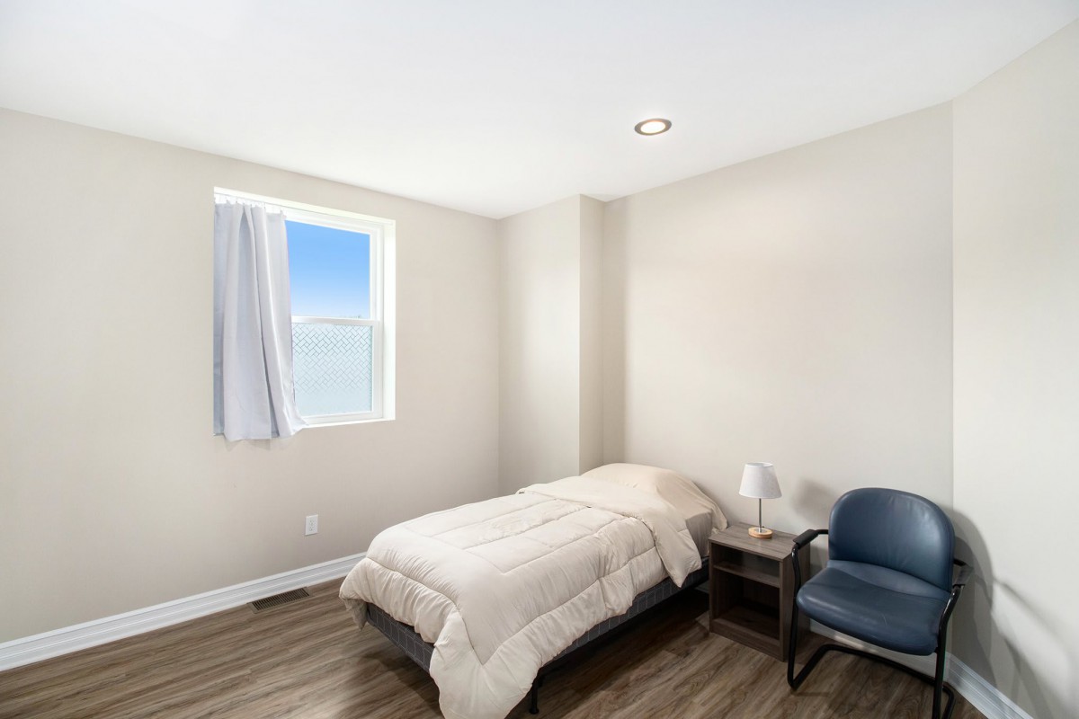 A minimalist bedroom with a single bed, wooden flooring, and ample natural light from the window.