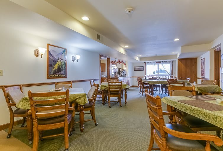 An inviting dining room with wooden tables and chairs arranged neatly, illuminated by overhead lighting.