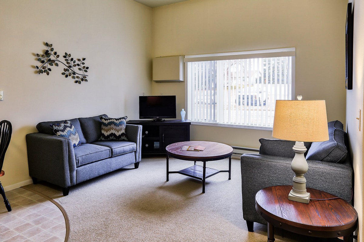 A cozy living room with a sofa, coffee table, and a large window allowing natural light.