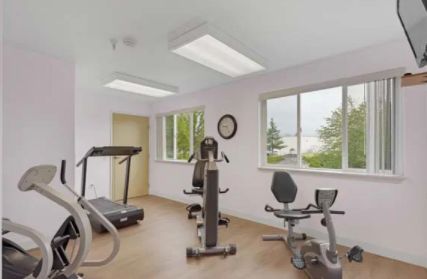 A compact home gym with various fitness equipment, including a treadmill and an exercise bike, set up in a well-lit room with windows.