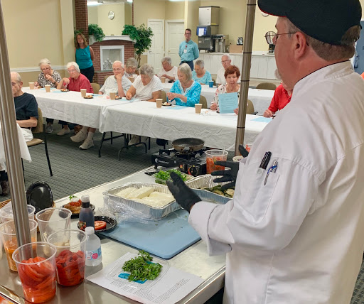 A chef conducts a cooking demonstration for an attentive audience of senior citizens.