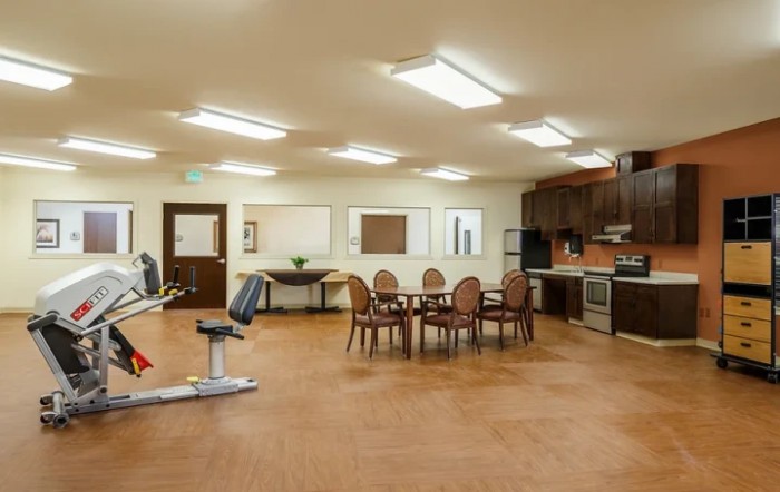 A spacious, well-lit fitness room with exercise equipment and a kitchen area.