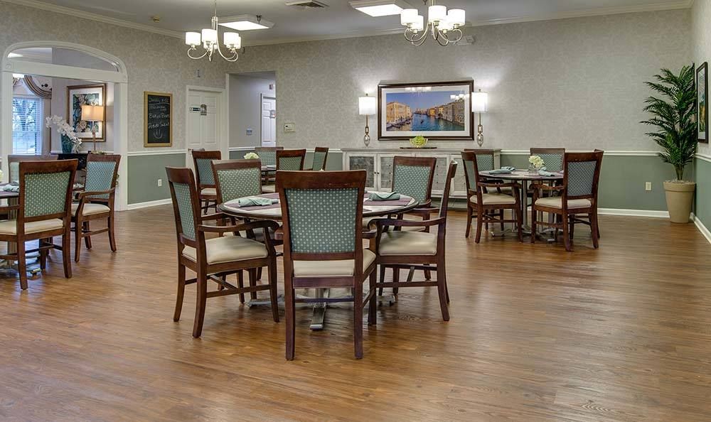 A spacious dining area with neatly arranged tables and chairs, featuring elegant chandeliers and wooden flooring.