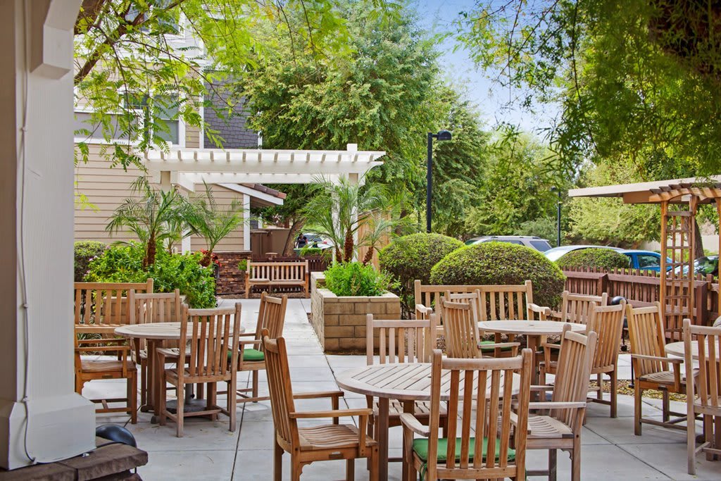 A charming outdoor patio area with wooden tables and chairs surrounded by lush greenery.